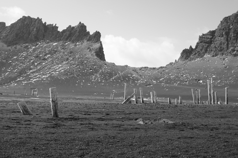 Black and white photo of two sets of jagged rocks forming a saddle.  Old fence posts in the foreground.   Reminiscent of a moonscape.