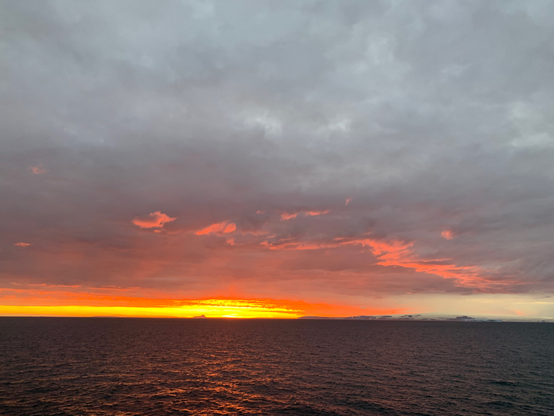 Bright orange sunset over the ocean against a backdrop of grey clouds.