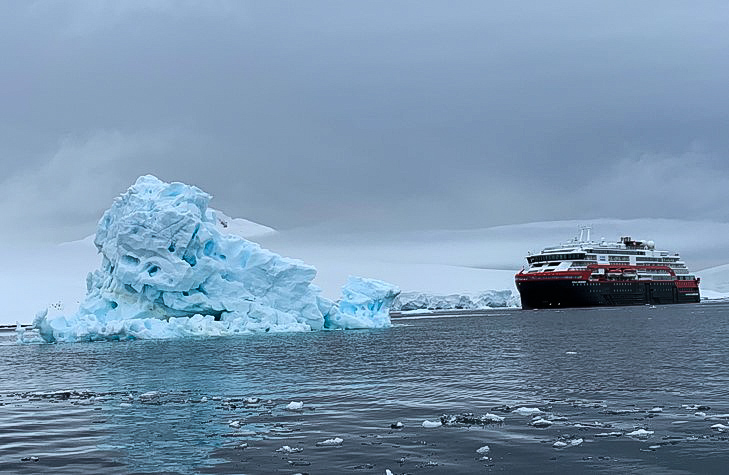 A black ship with red and white trim next to a giant, triangular, blue-tinted iceberg. 
