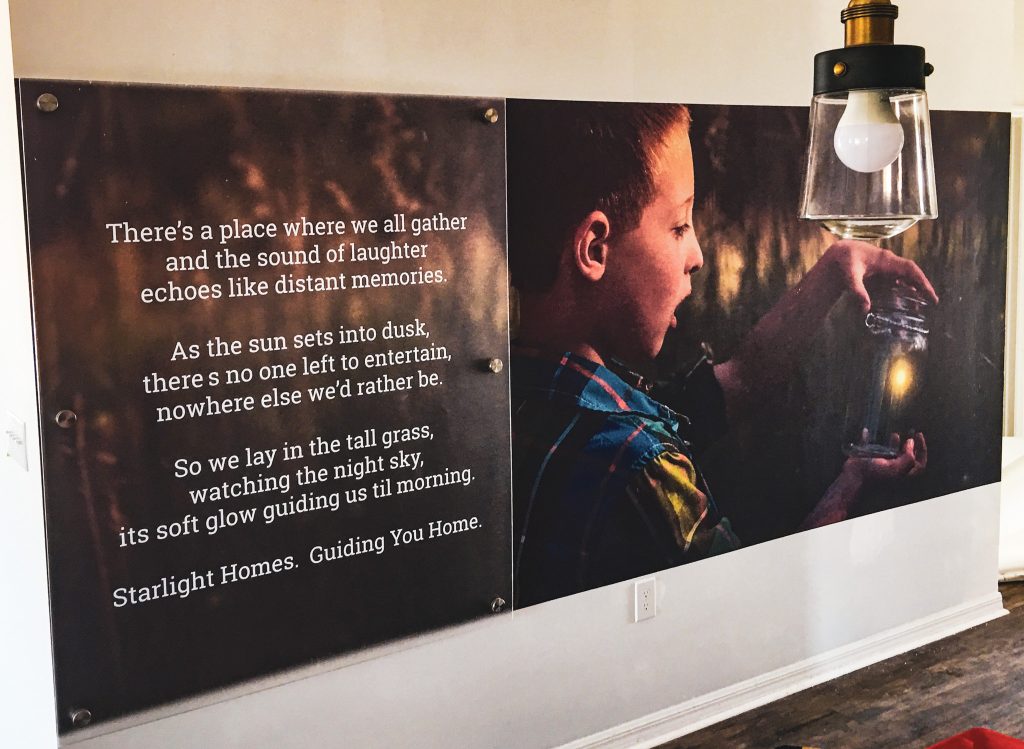 A wall wrap with the image of a boy capturing a firefly in a jar.  An acrylic panel with text overlays a portion of the wrap.  