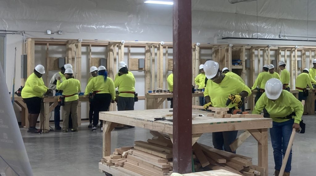 Students at the Home Building Academy practicing construction and electrical skills, against a backdrop of wood framing.