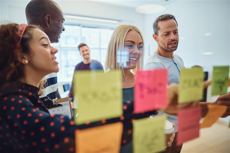 Stock Image of happy group of people using sticky notes on glass board for planning OKRs.