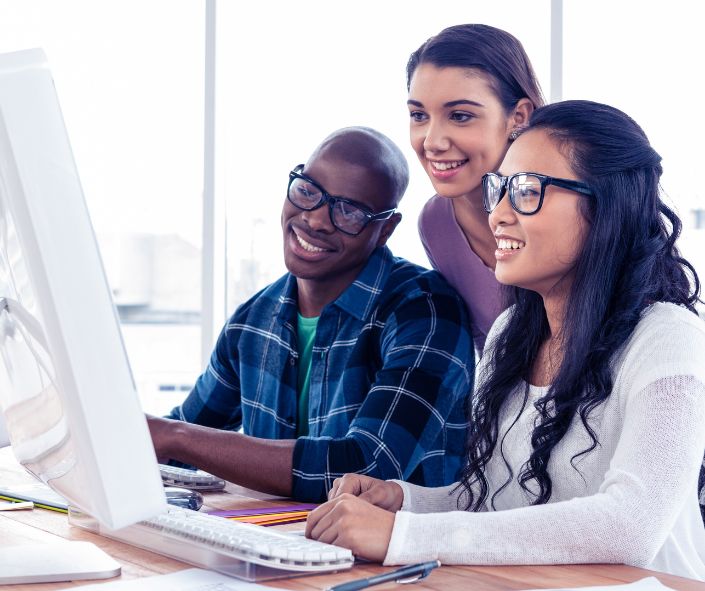 A young man and two young women collaborating in front of a computer screen.